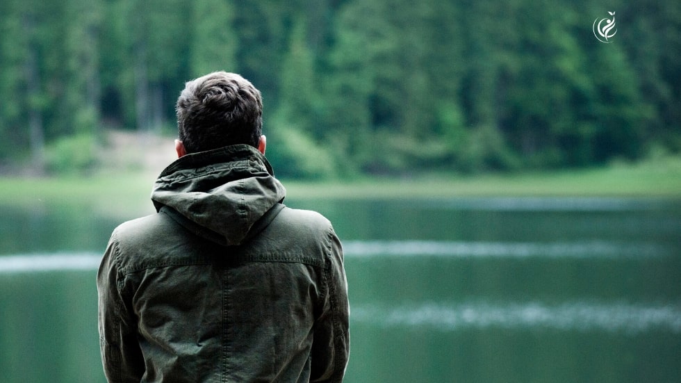 Mann sitzt am See und schaut auf den gegenüberliegenden Wald